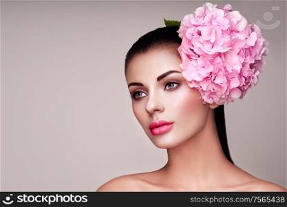 Portret model decorated with large pink flower on the head. Brunette woman with luxury makeup. Perfect skin. Eyelashes. Cosmetic eyeshadow