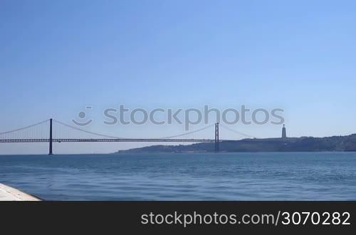 Portugal - der Fluss Tejo bei Lissabon mit der Brucke Ponte 25 de Abril und dem Christo Rei Denkmal in den Bergen bei blauem Himmel