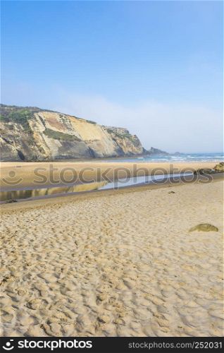 Portuguese Atlantic Ocean beach in the morning mist at sunrise. Breathtaking landscape and nature of the Portugal, popular travel destination in western Europe.