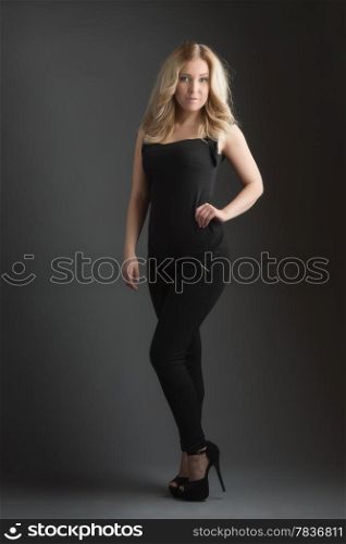 Posing beautiful blonde girl and looks at camera, dark background