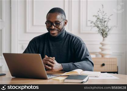 Positive African American ma≤private consu<ant having session onli≠listens to client attentively whi≤looking at computer screen with smi≤, working remotely from home office. Freelance concept. Positive African American ma≤private consu<ant having session onli≠listens to client attentively