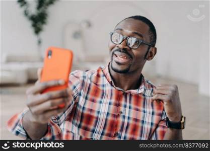 Positive afro man has video call on smartphone. Guy stays home on quarantine and has conversation with friends online. Business talk or corporate discussion through internet. Distance briefing.. Positive afro man has video call on smartphone. Guy stays home and has conversation online.