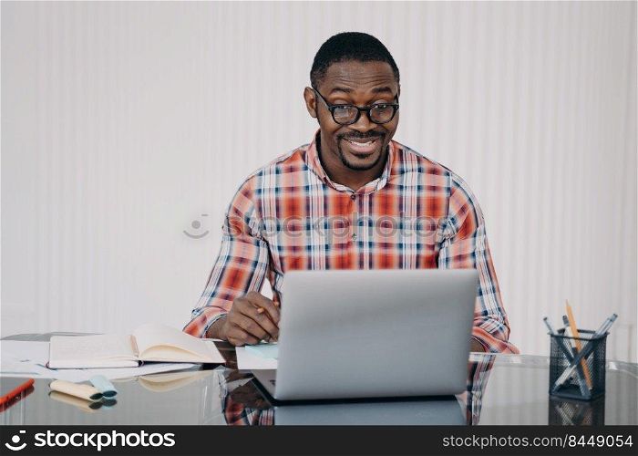 Positive afro man in glasses has online conference on laptop. Businessman gives consultation to client. Teacher has remote lesson with student. Online courses, internet meeting.. Businessman gives consultation to client. Teacher has remote lesson with student.