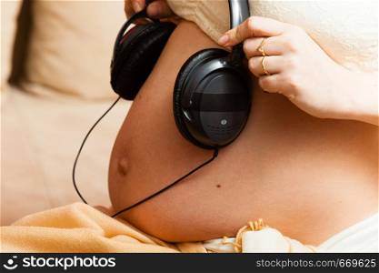 Positive aspects of baby listening to music concept. Woman with headphones on pregnant belly. Woman with headphones on pregnant belly