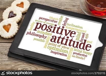 positive attitude word cloud on a digital tablet with a cup of tea and heart cookies