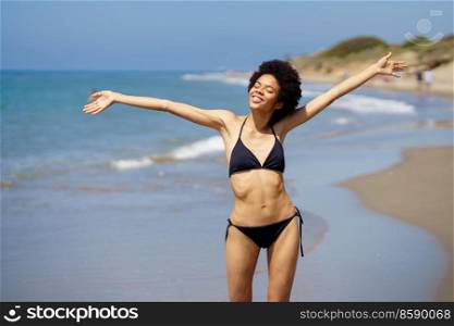 Positive black female opening her arms on the beach to enjoy her holiday in the sun.. Positive African American female opening her arms on the beach to enjoy her holiday in the sun.