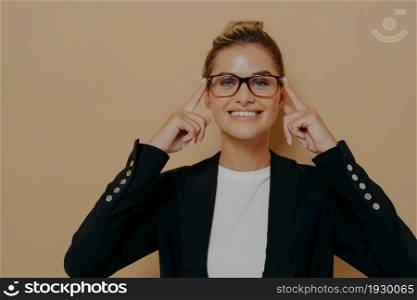Positive blonde female student putting on eyeglasses and holding them with hands, young beautiful caucasian woman posing and looking through spectacles at camera with beaming smile. Eyesight concept. Positive blonde female student putting on eyeglasses and holding them with hands