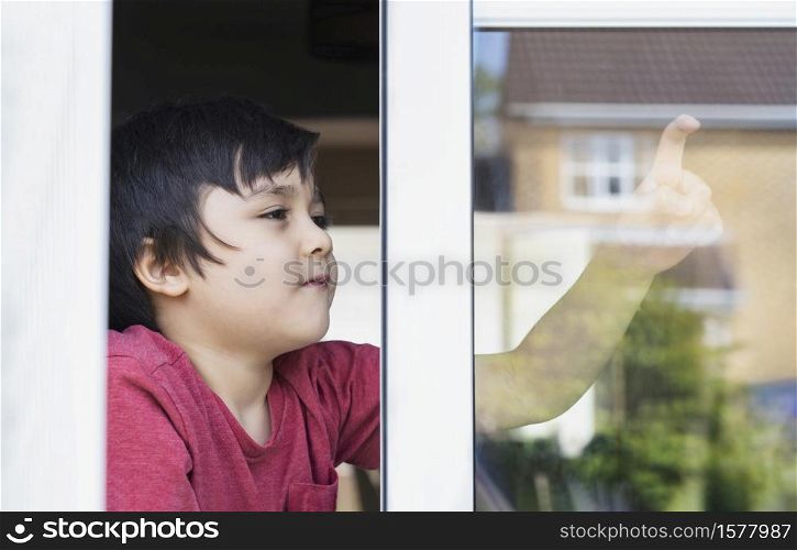 Positive child boy sitting at the window writing on glass with smiling face, School kid self isolation relaxing at home during covid 19, Home schooling , Distance education