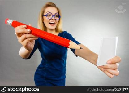 Positive crazy woman blonde student girl or female teacher, business coach holding huge red pencil and note paper, planning, having new idea. Studio shot on grey, wide angle view. Crazy woman holds big pencil in hand