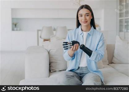 Positive disabled young woman sitting and disassembling bionic arm prosthesis. Cyber sensor artificial arm has processor chip and buttons. European girl has high tech carbon robotic hand and smiling.. Positive disabled young woman is disassembling bionic arm prosthesis and smiling.