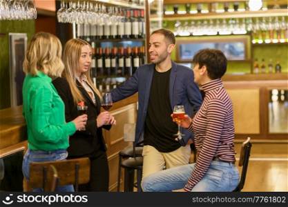 Positive diverse man and women in casual clothes smiling and listening to girlfriend while drinking alcohol in bar together. Friends talking during meeting in a nice pub