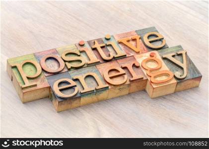 positive energy word abstract in letterpress wood type against grained wood