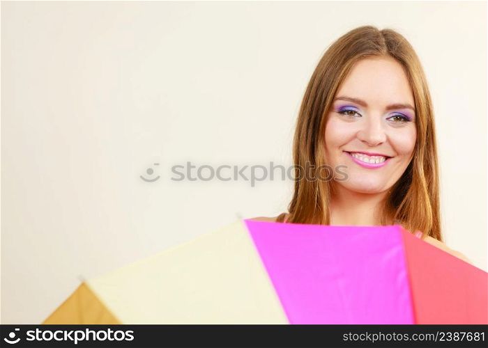 Positive face expression concept. Shy attractive smiling woman hiding behind colorful umbrella. Shy woman hiding behind colorful umbrella