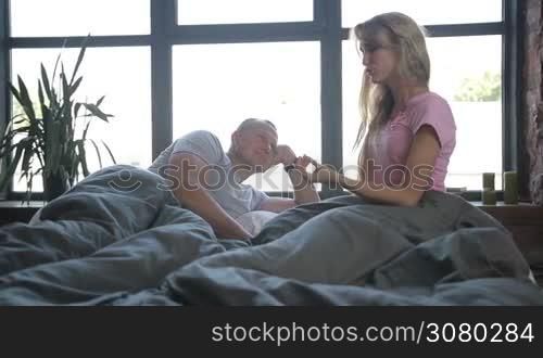 Positive family with adorable curly girl spending leisure in bedroom after awakening. Happy child with cheerful parents enjoying great time together in bed in the morning. Slow motion. Dolly shot. People family and morning concept.
