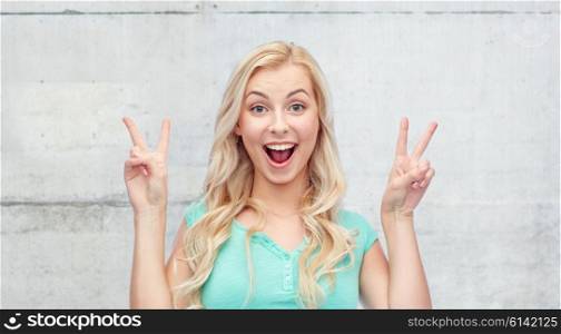 positive gesture and people concept - smiling young woman or teenage girl showing peace hand sign with both hands over gray concrete wall background. smiling young woman or teenage girl showing peace