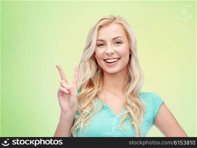 positive gesture and people concept - smiling young woman or teenage girl showing peace hand sign over green natural background. smiling young woman or teenage girl showing peace