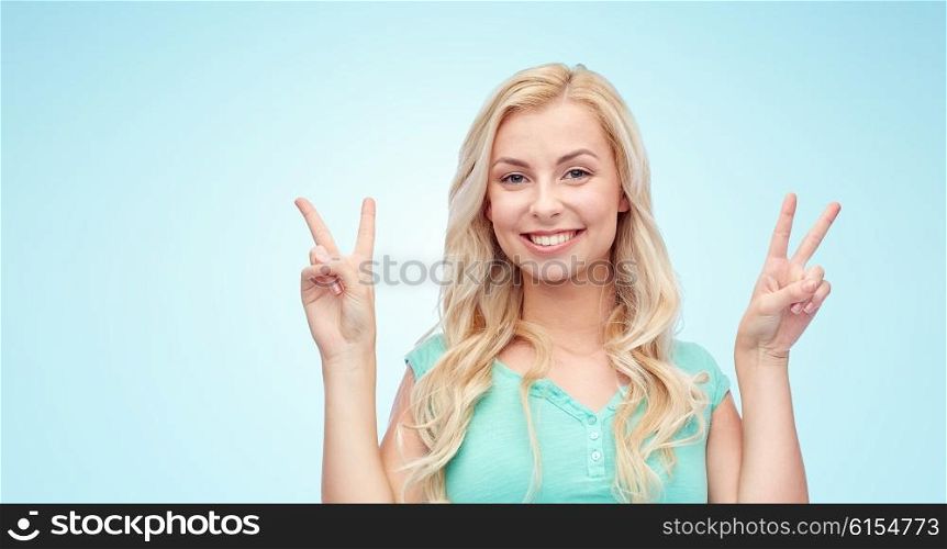 positive gesture and people concept - smiling young woman or teenage girl showing peace hand sign with both hands over blue background. smiling young woman or teenage girl showing peace