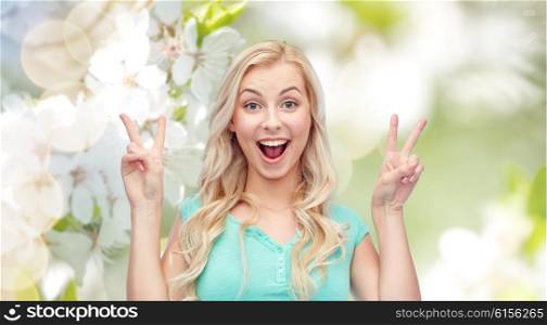 positive gesture and people concept - smiling young woman or teenage girl showing peace hand sign with both hands over natural spring background. smiling young woman or teenage girl showing peace