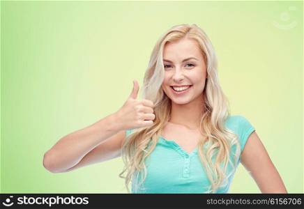 positive gesture and people concept - smiling young woman or teenage girl showing thumbs up over green natural background. happy woman or teenage girl showing thumbs up