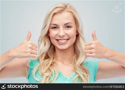 positive gesture and people concept - smiling young woman or teenage girl showing thumbs up with both hands over gray background. happy woman or teenage girl showing thumbs up