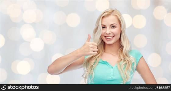 positive gesture and people concept - smiling young woman or teenage girl showing thumbs up over holidays lights background. happy woman or teenage girl showing thumbs up