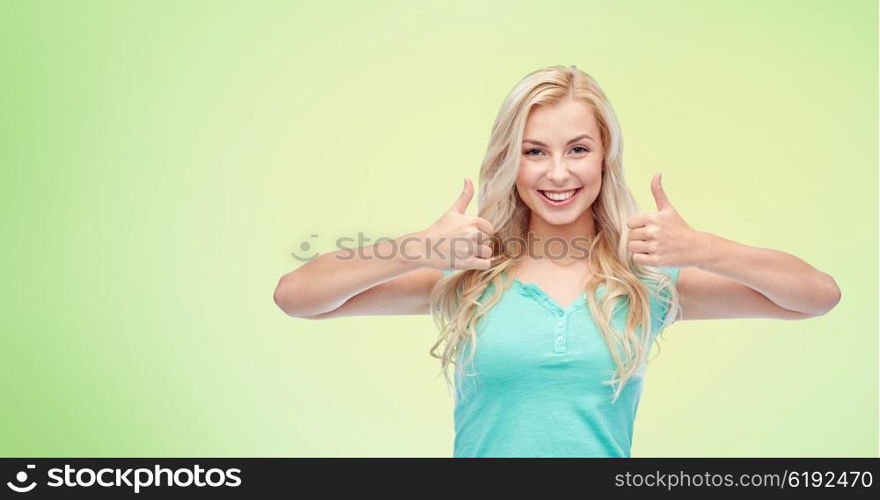 positive gesture and people concept - smiling young woman or teenage girl showing thumbs up with both hands over green natural background. happy woman or teenage girl showing thumbs up