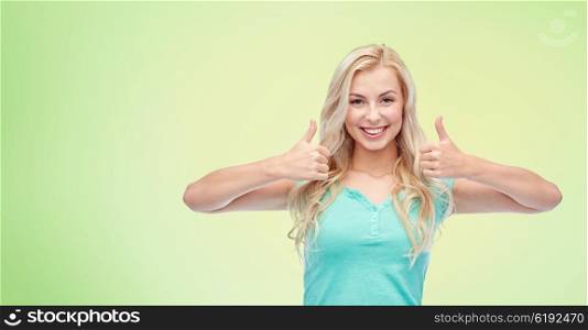 positive gesture and people concept - smiling young woman or teenage girl showing thumbs up with both hands over green natural background. happy woman or teenage girl showing thumbs up