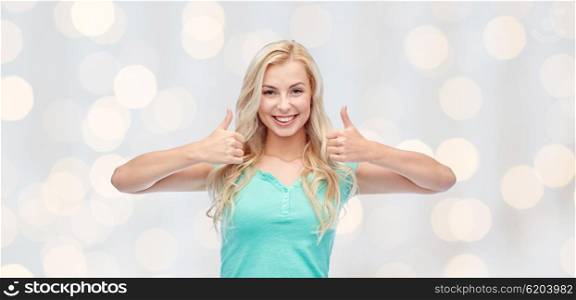 positive gesture and people concept - smiling young woman or teenage girl showing thumbs up with both hands over holidays lights background. happy woman or teenage girl showing thumbs up