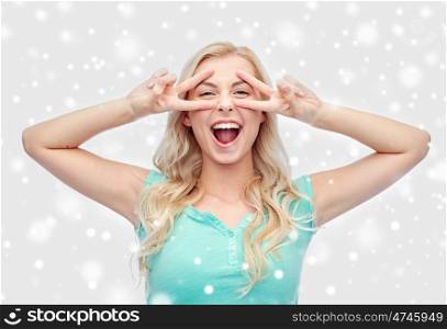 positive gesture, emotion, winter holidays, christmas and people concept - smiling young woman or teenage girl showing peace hand sign with both hands over snow