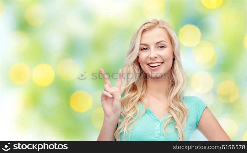 positive gesture, summer and people concept - smiling young woman or teenage girl showing peace hand sign over green lights background