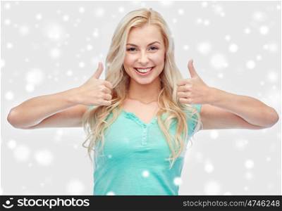 positive gesture, winter holidays and people concept - smiling young woman or teenage girl showing thumbs up with both hands over snow
