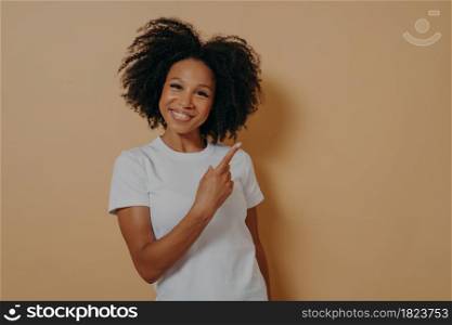 Positive good looking african female model in white shirt indicating with forefinger at blank copy space and smiling, pointing at right upper corner. Advertisement and promotion concept. Positive young african female model in white shirt indicating with forefinger at blank copy space