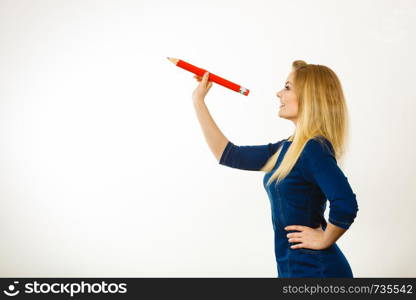 Positive smiling woman blonde student girl or female teacher holding big red pencil drawing. Studio shot on white.. Positive woman holds big pencil in hand