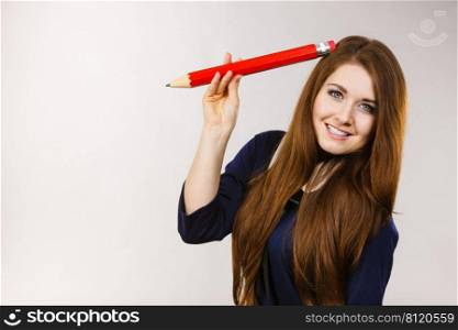 Positive smiling woman long hair student girl or female teacher holding big red pencil drawing. Studio shot on grey. Smiling woman holds big pencil in hand