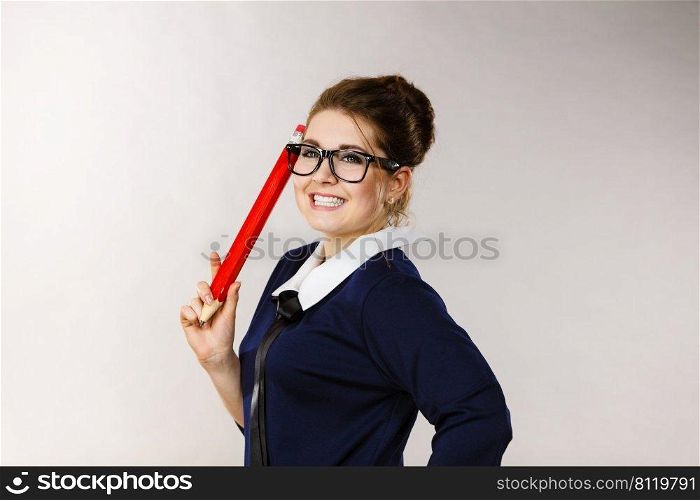 Positive smiling woman student girl or female teacher holding big red pencil drawing. Studio shot on grey. Smiling woman holds big pencil in hand