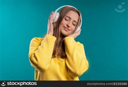 Positive woman listening music, enjoying with headphones on blue studio background. Radio, wireless modern sound technology, online player. High quality. Positive blonde woman listening music, enjoying headphones on blue background.