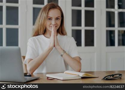 Positive woman sitting with her hands folded and relaxing. Successful young blond businesswoman is working at computer. Lovely european lady has remote work in her apartment. Concept of confidence.. Positive woman sitting with her hands folded and relaxing. Successful young blond businesswoman.
