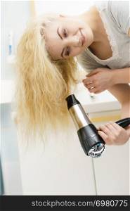Positive woman using hair dryer on her blonde hairdo. Haircare, hairstyling concept.. Blonde woman using hair dryer