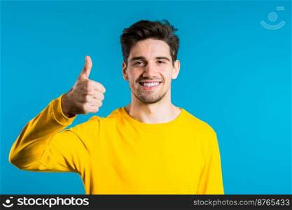 Positive young man smiles to camera. Hipster guy showing thumb up sign over blue background. Winner. Success. Body language. Positive young man smiles to camera. Hipster guy showing thumb up sign over blue background. Winner. Success. Body language.