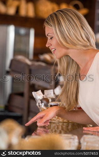 Positive young woman at the bakery store choosing what she wants to by and placing order to seller