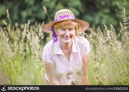 Positivity. Happy Senior Peasant Woman in Meadow smiling. Mature Friendly Lady in Bonnet