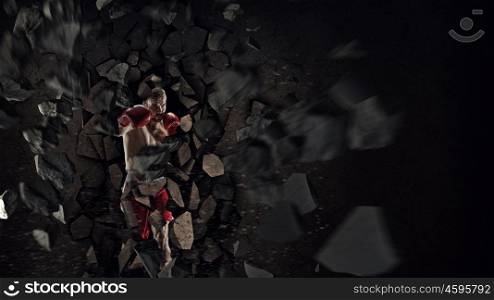 Possessing power and endurance. Strong boxer man in gloves breaking cement wall
