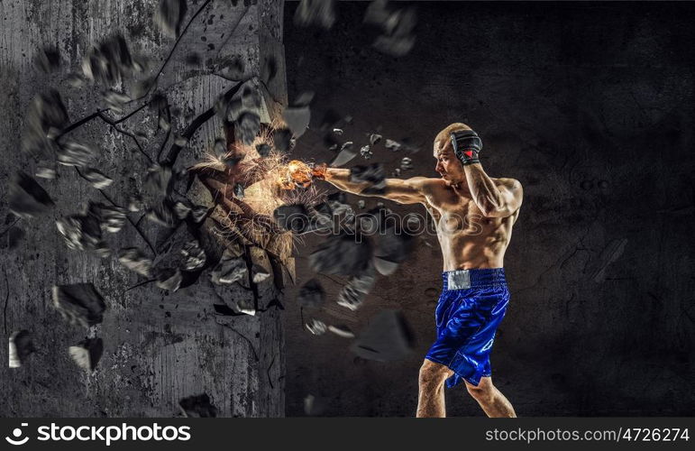 Possessing power and endurance. Strong boxer man in gloves breaking cement wall