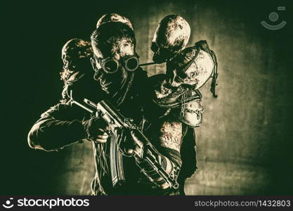 Post apocalyptic survivor, radioactive zone stalker, crazy serial killer or maniac in glasses and skulls on shoulders, with automatic rifle. Nuclear post-apocalypse creature brandishing ax