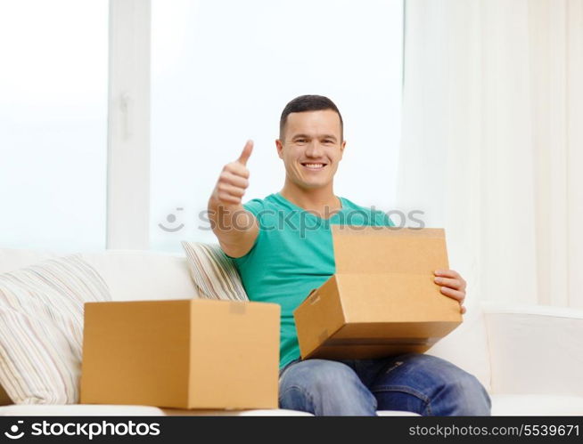 post, home and lifestyle concept - smiling man with cardboard boxes at home showing thumbs up