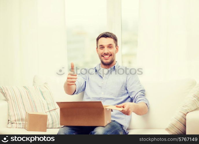 post, home and lifestyle concept - smiling man with cardboard boxes at home showing thumbs up