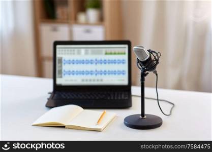 post production and technology concept - microphone, laptop computer with sound editor program, headphones and notebook on table at home office. microphone, laptop and notebook on table