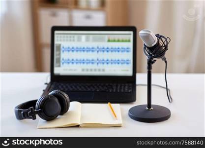 post production and technology concept - microphone, laptop computer with sound editor program, headphones and notebook on table at home office. microphone, laptop, headphones, notebook on table