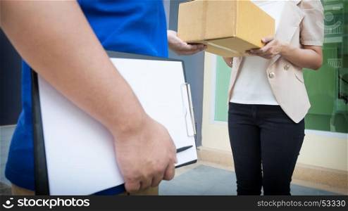 Postal - delivery of a package through a service; Woman customer hand accepting receipt cardboard box while young deliveryman holding clipboard.