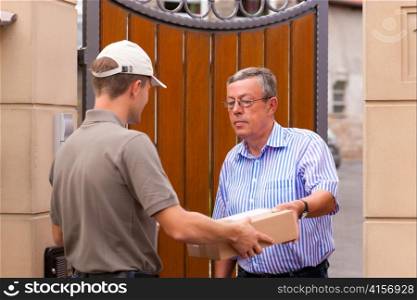 Postal service - delivery of a package; the postman is giving the package to the customer in front of his house